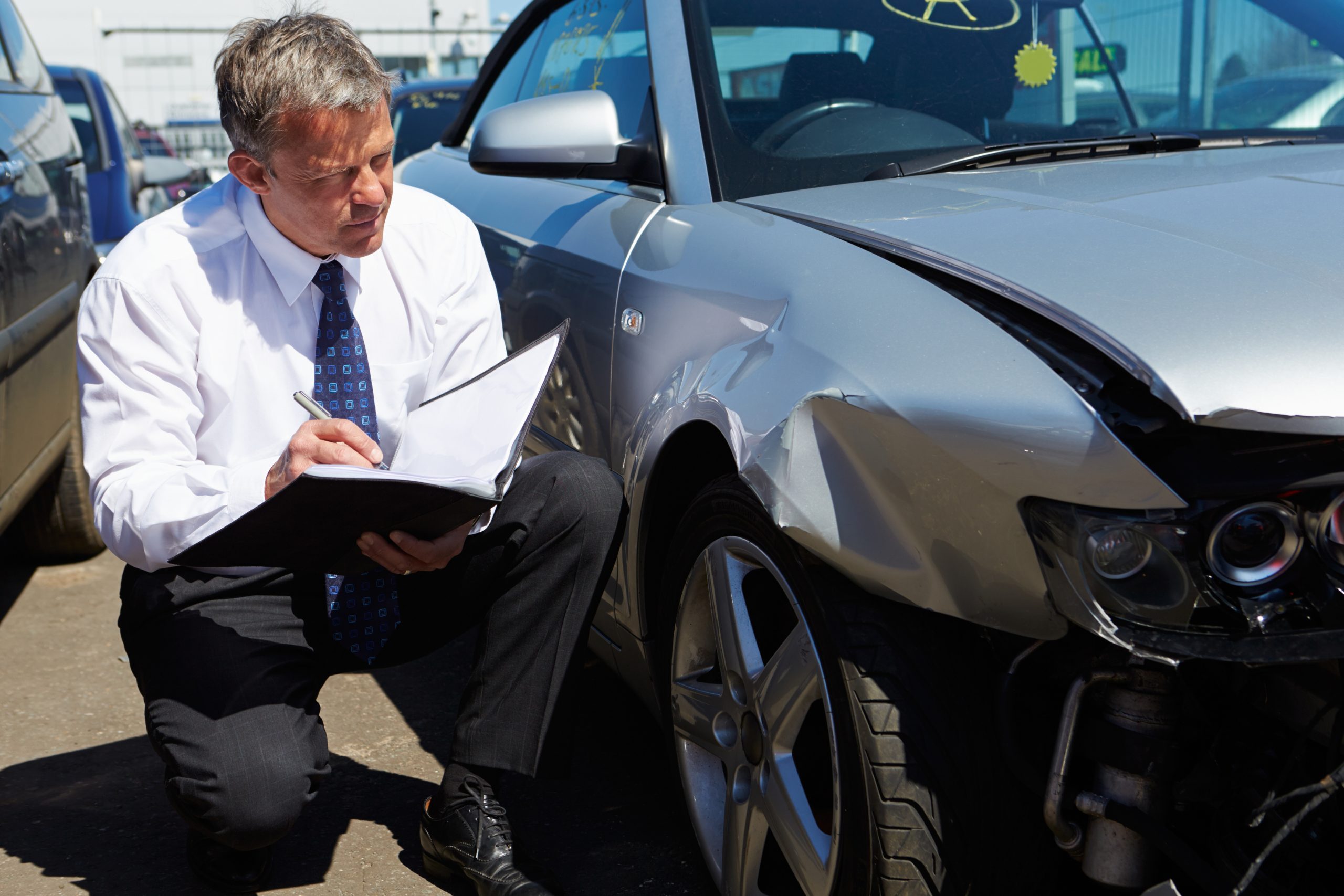 Man inspecting a damaged silver car.